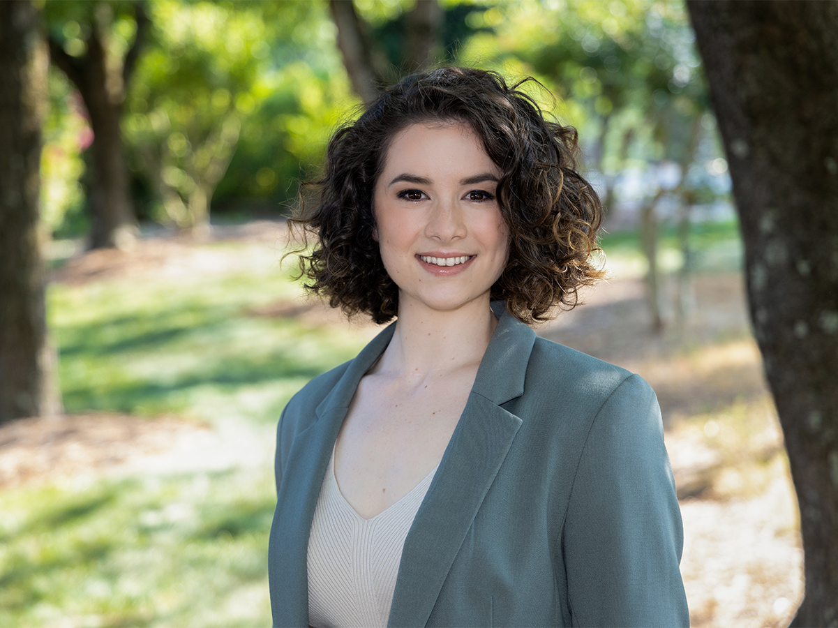 Headshot of Alissa Bodden. She has short curly hair and is wearing a blazer, smiling and standing outside.